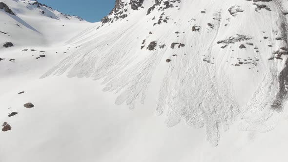 Aerial: flying close to snow avalanche on mountain snowy slope reveals in springtime alt