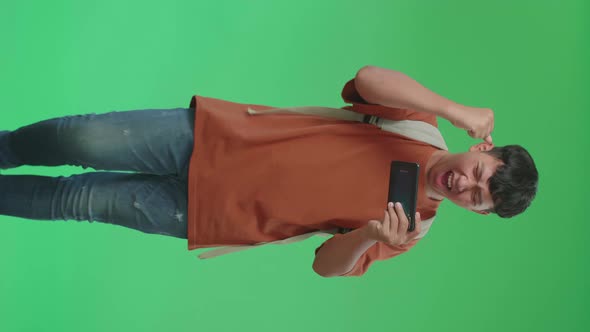 The Front View Of Asian Boy Student Wining The Game On Mobile Phone While Walking On Green Screen