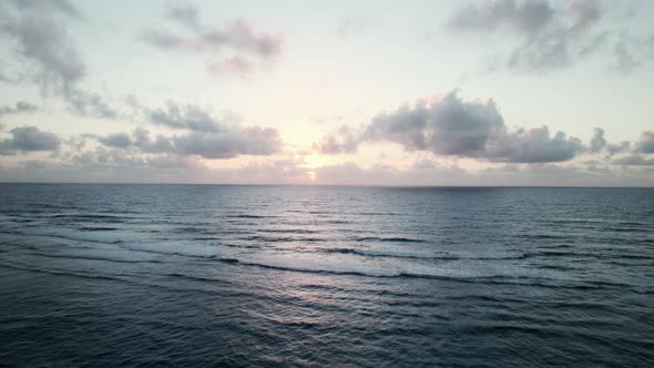 Calm open ocean as the morning sun illuminates large clouds on the distant horizon, aerial