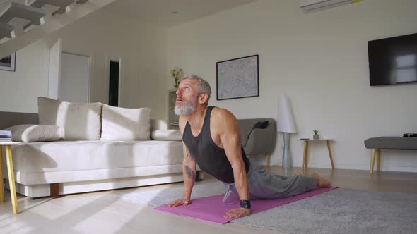 Fit Tattooed Mature Man Doing Morning Workout Yoga Exercise at Home