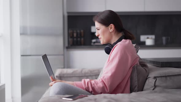 Caucasian Woman at Home Sitting at Kitchen Sofa Making Video Call on Laptop Wearing Headphones