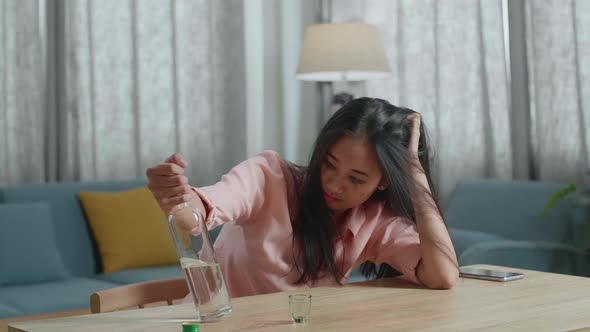 Drunk, Depressed Asian Woman With Smartphone On Table Drinking Vodka From The Bottle At Home
