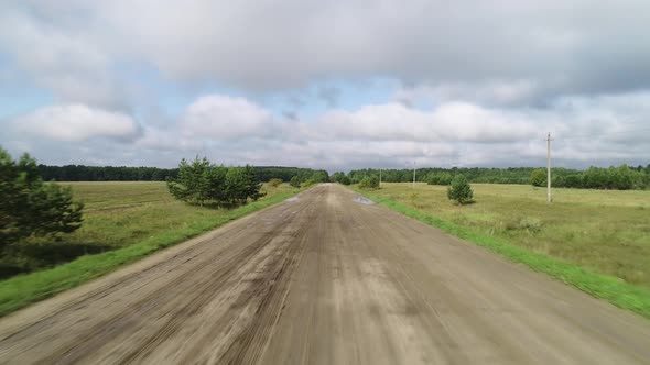 Flying Over a Dirt Rural Road Running Through Green Fields.