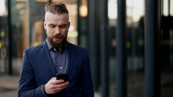 a Mustachioed and Bearded Man in a Plaid Jacket Looks Discontentedly at the Phone Screen and Walks