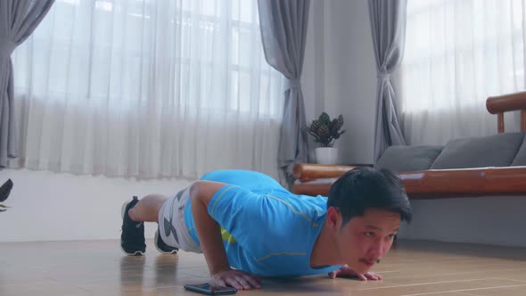 Asian Man Doing Push Up Exercises While Using A Stopwatch On His Phone