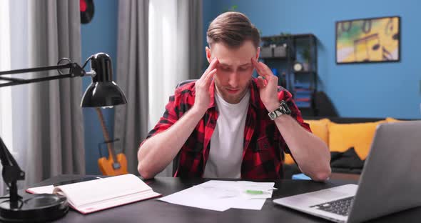 A Tired Young Man Sits at His Desk in His Room and Reviews His Apartment