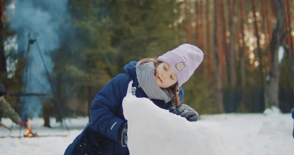 Cute Girl Builds and Plays in the Snow in the Forest