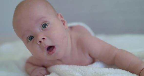 Close Portrait of Funny Reaction Into Camera of Cute Newborn Baby on Bed