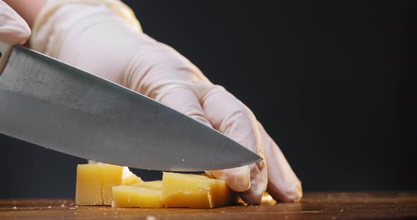 Person Cuts Natural Cheese Into Cubes with Knife on Board