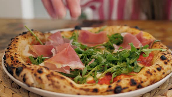 Chef in the Pizzeria Prepares a Pizza and Decorates It with Prosciutto. Green Herbs Close Up