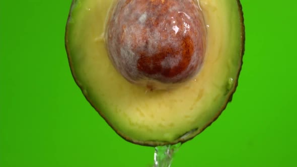 Water falling from avocado on green background. Avocado slice and water splashing, drops of juice