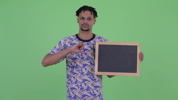 Serious Young African Man Holding Blackboard and Giving Thumbs Down