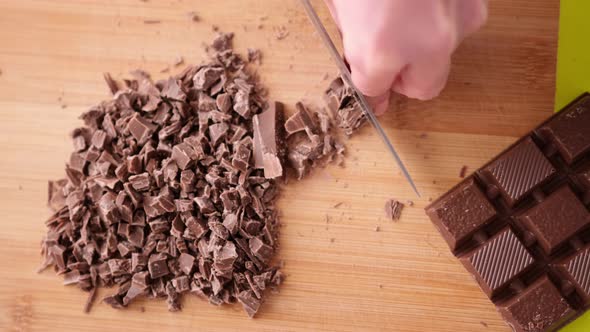 Woman Chopping Black Dark Chocolate on Wooden Cutting Board