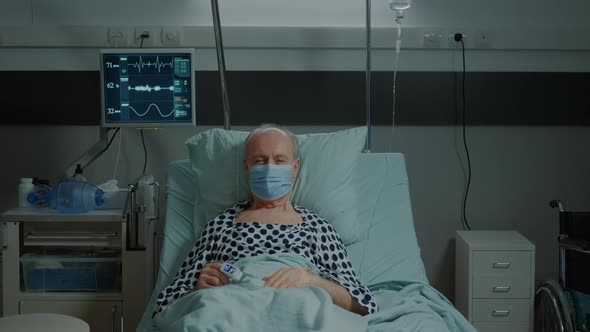 Portrait of Old Patient with Face Mask Sitting in Hospital Ward