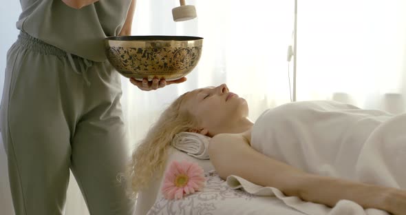 Relaxed Woman Lies Under Towel Listening To Tibetan Bowl