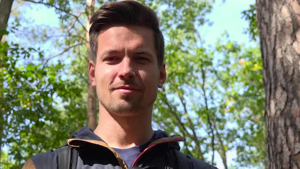 A Young Handsome Backpacker Smiles at the Camera in a Forest, Face Closeup From Below