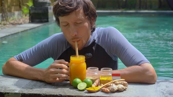 A Young Man Drinks the National Balinese Drink Jamu Swimming in the Swimming Pool