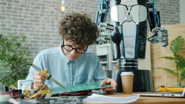 Female Engineer Soldering Robot Motherboard with Solderer in Modern Office