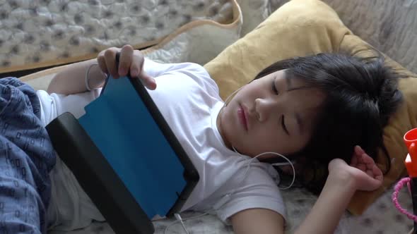 Asian Bored Boy Using Tablet While Lying On Bed