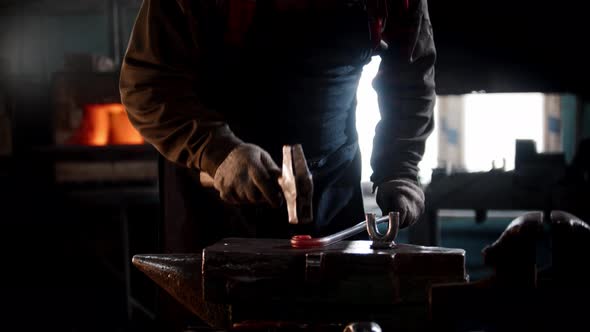 Blacksmith Workshop  a Man Bends a Piece of Metal with Hitting It with a Hammer on Anvil