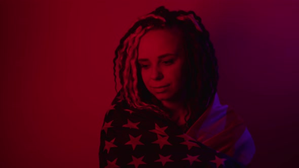 Young Woman Wrapped in American Flag on Red Background in Dark Room at Night