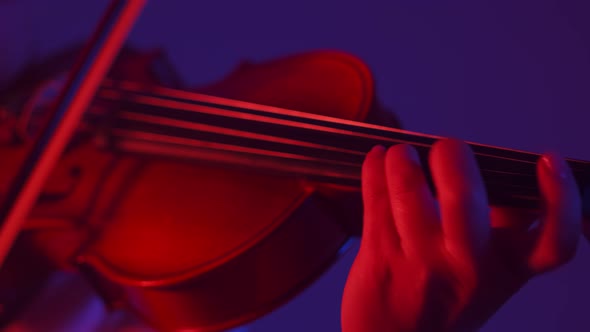 Violinist Woman Plays with Fingers and Bow on the Strings of the Violin in Red Light Studio Closeup