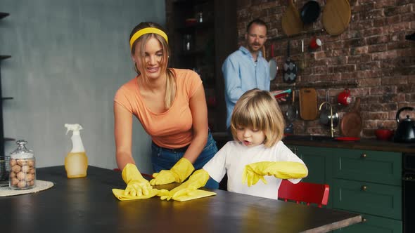 Mum and Her Little Child Boy in Yellow Rubber Gloves are Smiling and Talking Wiping Table By Rags