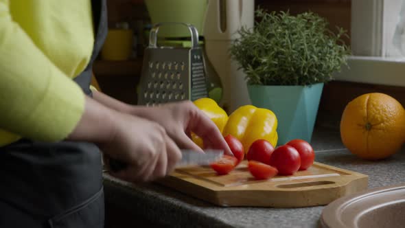 Housewife in Apron Cuts Cherry Tomatoes with a Knife on a Wooden Board