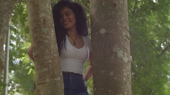 Sexy latina woman standing in the middle of two tree trunk while smiling