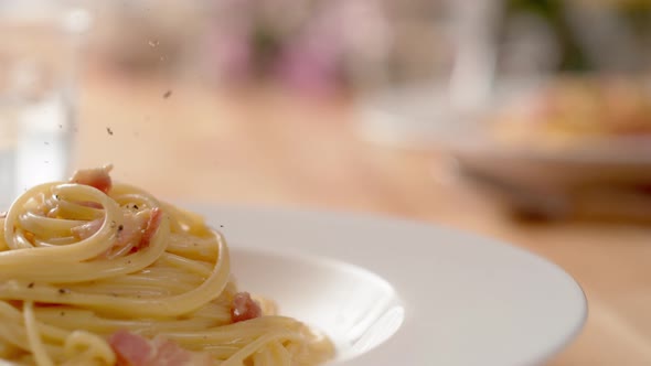 Camera follows grinding pepper over carbonara pasta. Slow Motion.