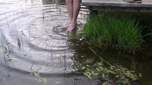 a man sitting on the edge of a wooden jetty, swinging one's feet near the water