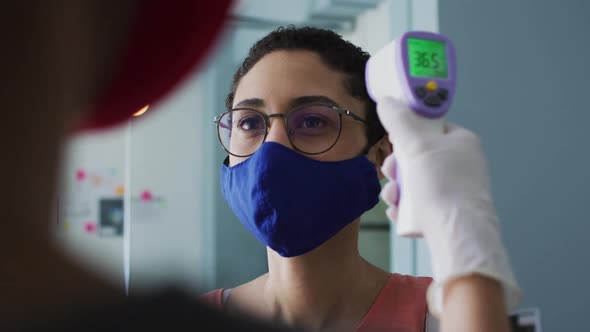 Caucasian woman wearing face mask getting her temperature measured at modern office
