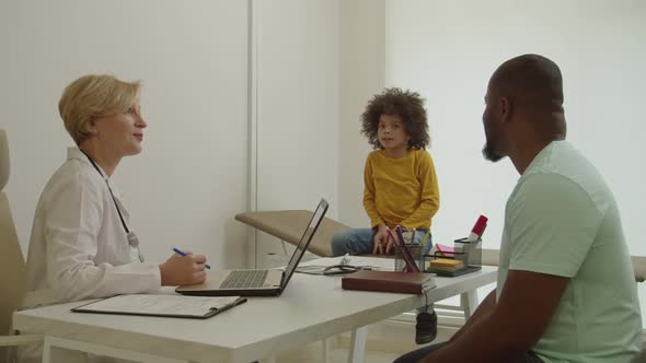 Sick Adorable Little African American Boy Telling Female Pediatrician About Symptoms of Illness