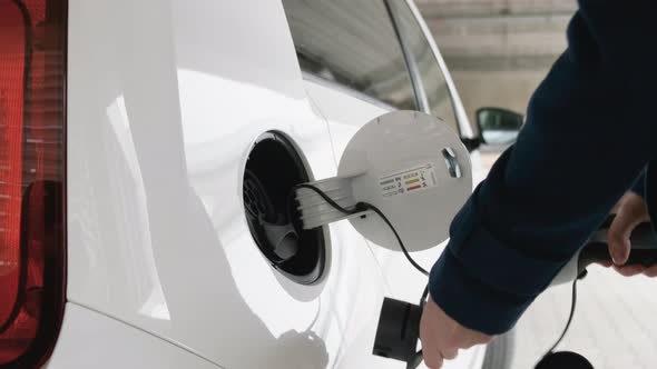 Business Woman Inserting a Charger Into the Electric Car at Charging Point in the Parking
