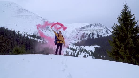 A Man with a Backpack Waving Pink Smoke Bomb in the Mountains in Winter