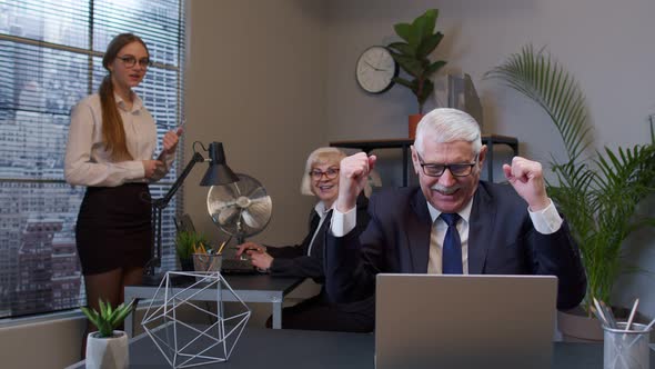 Cheerful Mature Old Businessman Raising Hands Celebrating Sudden Victory with Colleagues in Office