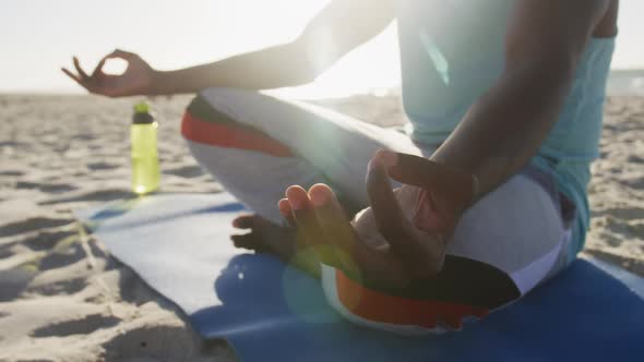 Midsection of african american man practicing yoga on beach, exercising outdoors by the sea