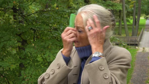 An Elderly Woman Combs Her Hair in a Park - Closeup