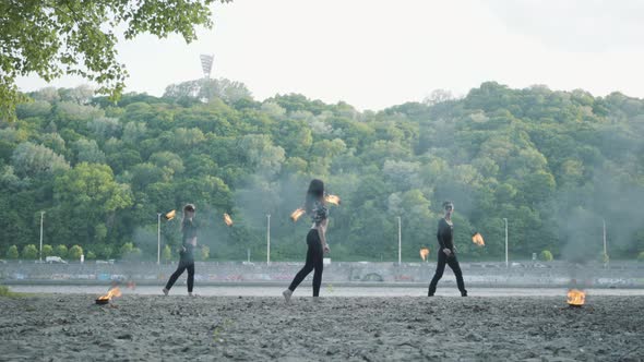 Young Slim Man and Two Beautiful Women Simultaneously Perform Show with Flame While Standing in