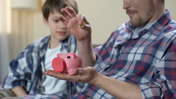 Father and Son Putting Coin Into Piggy Bank and Giving High Five, Save for Dream