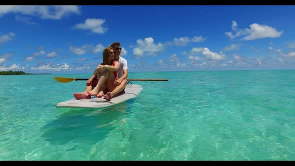 Two lovers tanning on relaxing coastline beach trip by aqua blue ocean with white sandy background o