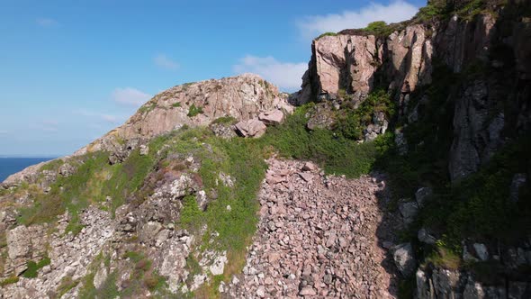 Drone flying forward, upwards and close to cliffs, revealing forest, Kullaberg Sweden