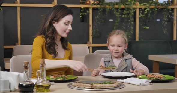 Beautiful Young Caucasian Mother Putting Pizza on Plate of Cute Daughter