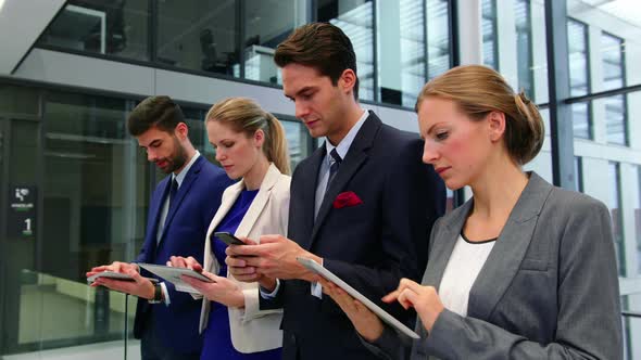 Business executives using mobile phone and digital tablet in corridor