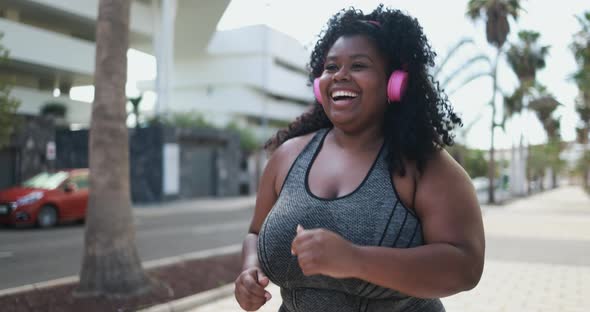 Curvy african woman running outdoor while listening music from playlist -