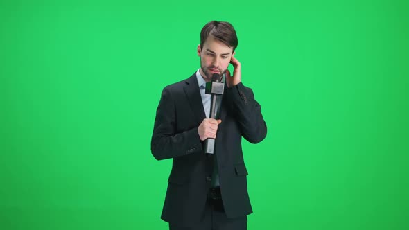 Young Man Reporter in Suit Looks Into the Camera and Speaks Into a Microphone on a Green Background