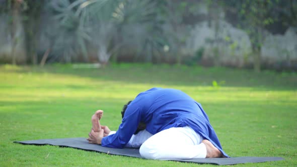 Indian man doing Folded leg forward bend yoga or Triang Mukha Eka Pada Paschimottanasana