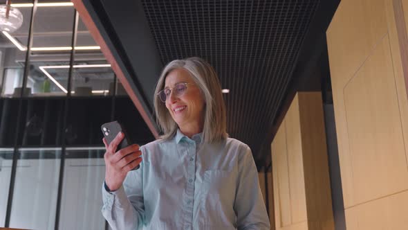 Grayhaired Senior Businesswoman is Using a Smartphone in an Office