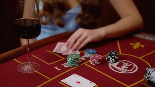 A modern woman dressed in blue with a glass of wine on the table checks her cards during a poker mat