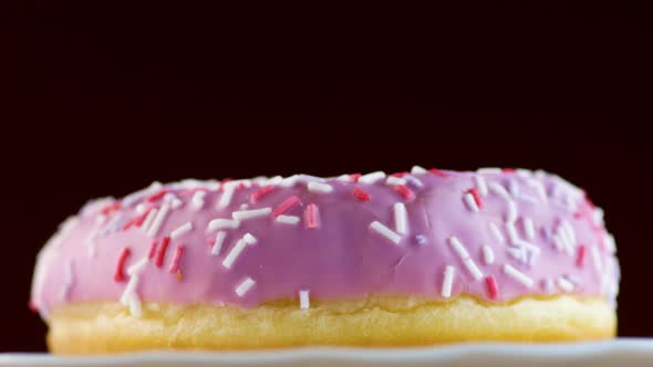 Delicious pink donut on a plate rotates on a black background.